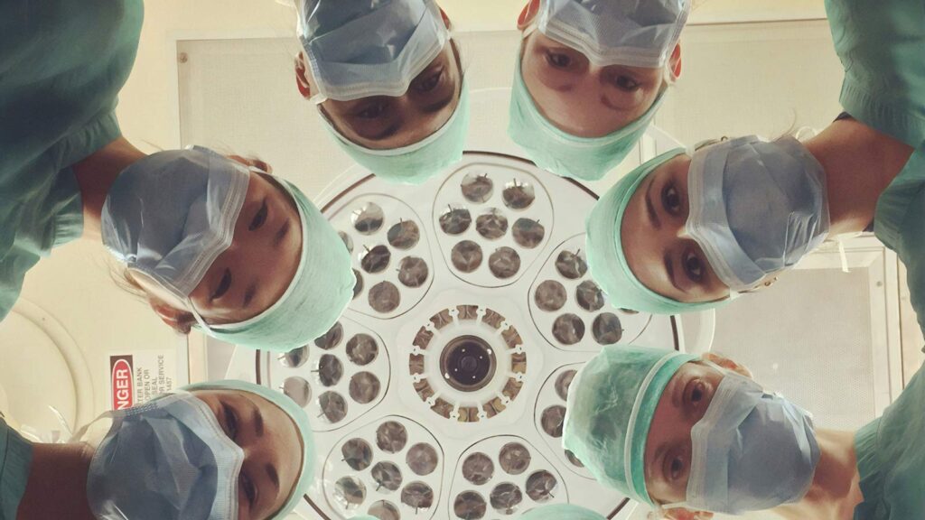 Five medical professionals wearing scrubs and masks looking down at the camera in what appears to b...